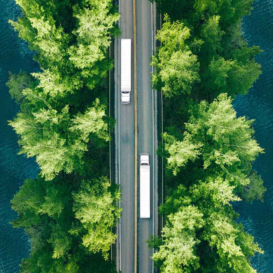 Aerial view of two semi trucks passing on a highway in the green summer woods